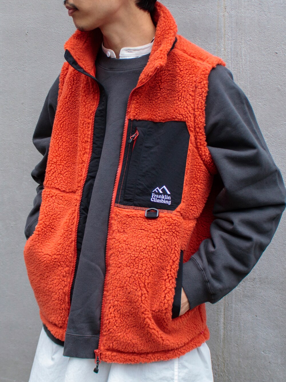 オレンジ系のベスト、グレー系のスウェット、ベージュ系のサンダルを着用したメンズの秋コーディネートの2枚目の写真