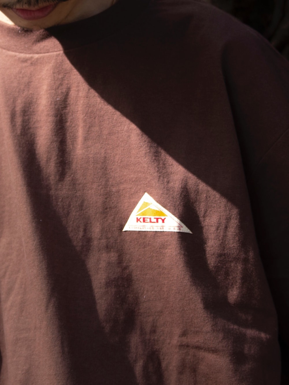 ブラウン系のTシャツ/カットソー、ホワイト系のその他パンツ、ブラック系のショルダーバッグを着用したメンズの春コーディネートの2枚目の写真