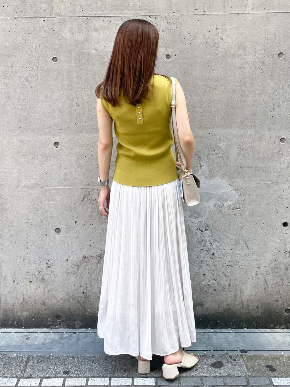 イエロー系のニット/セーター、ベージュ系のショルダーバッグ、グレー系のスカートを着用したレディースの夏コーディネートの2枚目の写真