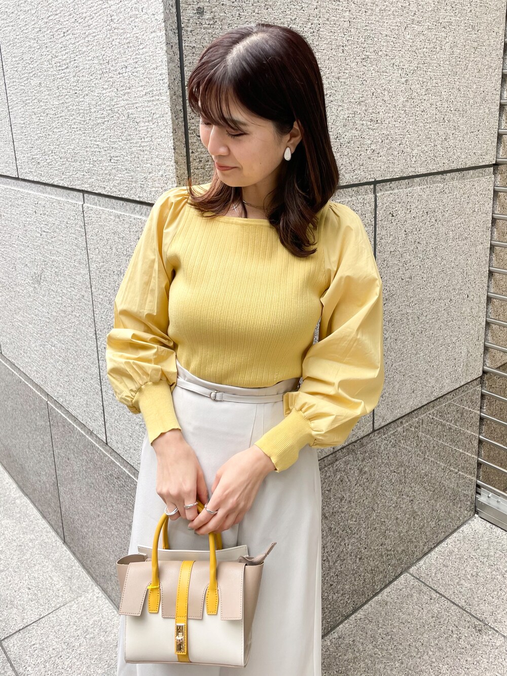 イエロー系のニット/セーター、グレー系のスカート、イエロー系のショルダーバッグを着用したレディースの春コーディネートの3枚目の写真