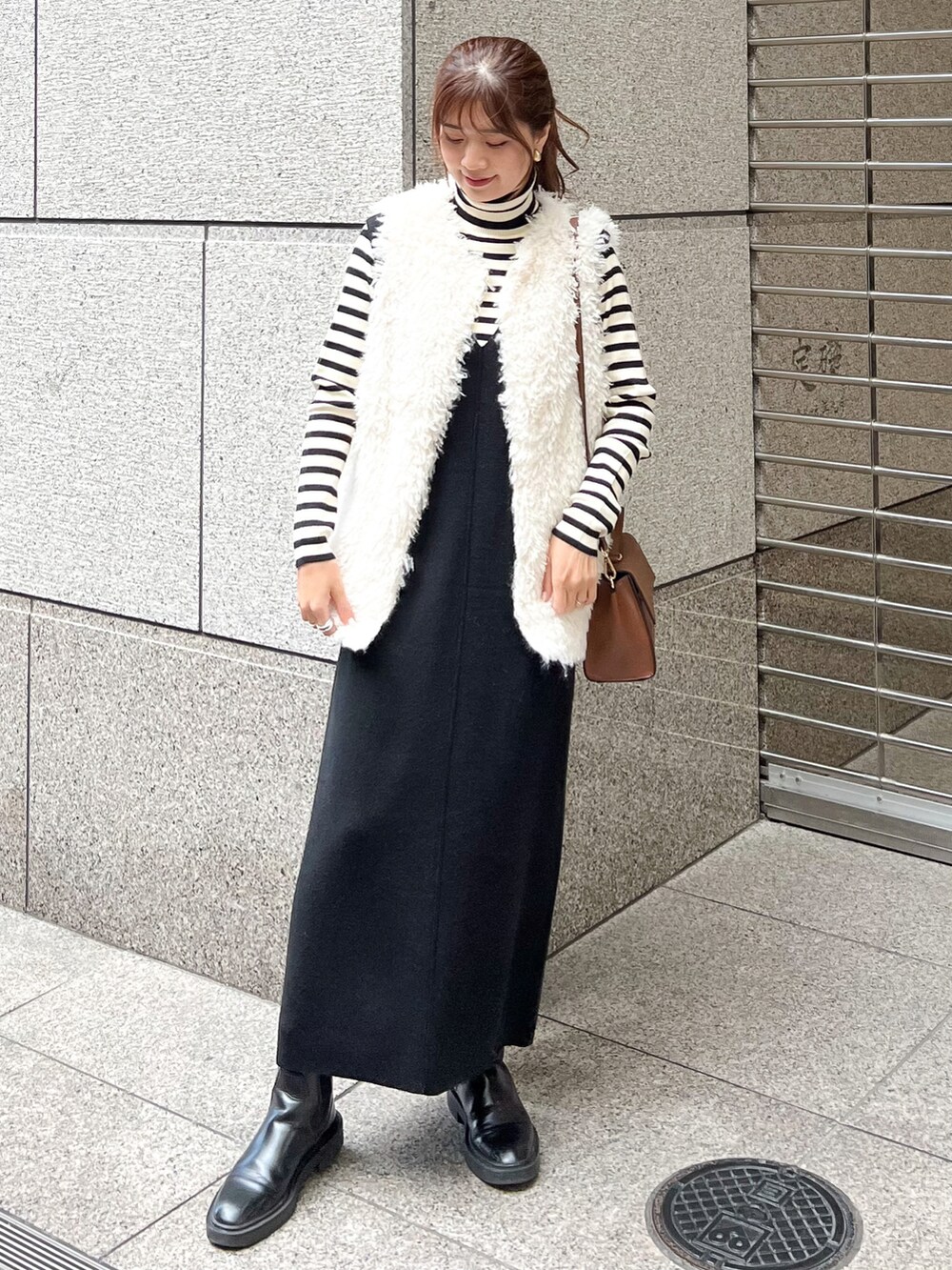 ブラック系のジャンパースカート、ホワイト系のニット/セーター、ホワイト系のベストを着用したレディースの秋コーディネートの2枚目の写真