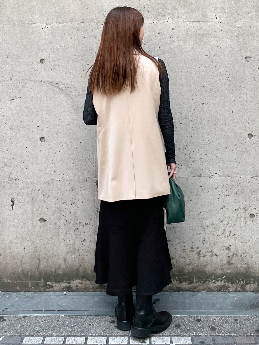 グリーン系のTシャツ/カットソー、ブラック系のスカート、ベージュ系のベストを着用したレディースの秋コーディネートの2枚目の写真