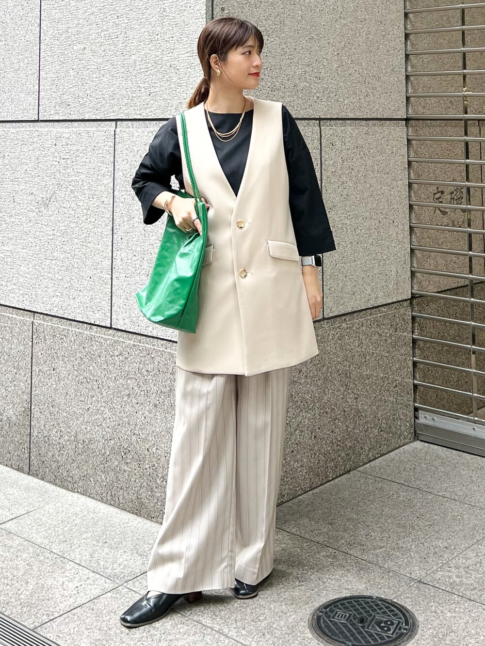 ブラック系のTシャツ/カットソー、ベージュ系のベスト、グリーン系のトートバッグを着用したレディースの春コーディネートの2枚目の写真