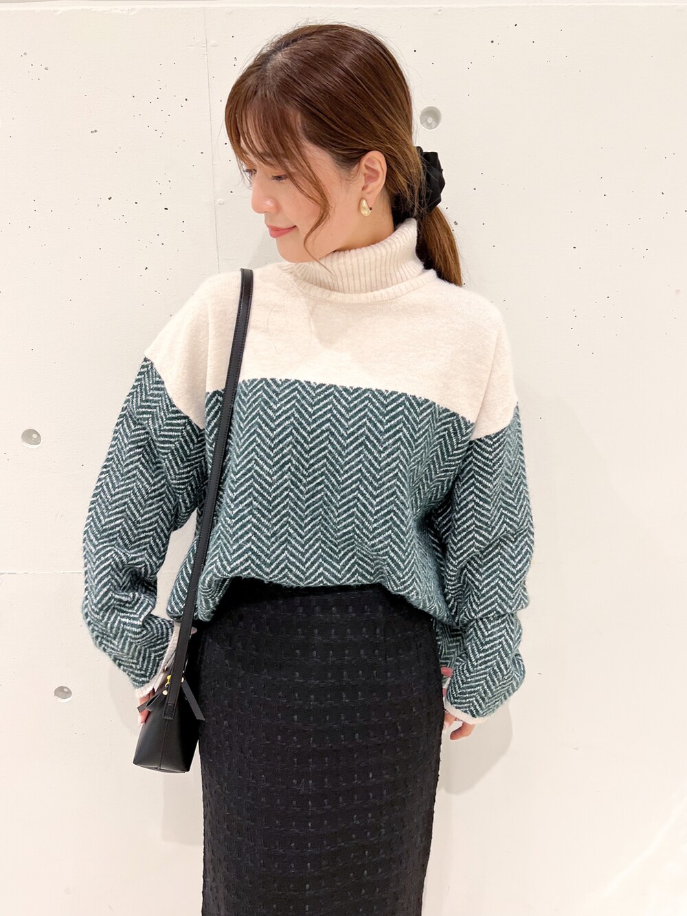 グリーン系のニット/セーター、ブラック系のスカート、ブラック系のショルダーバッグを着用したレディースの秋コーディネートの3枚目の写真