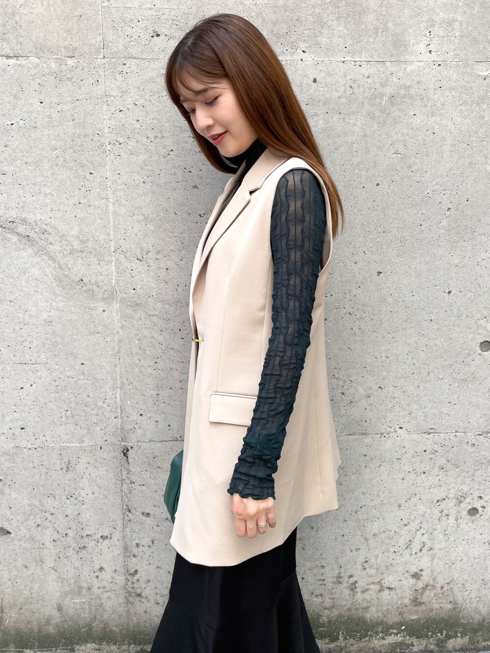 グリーン系のTシャツ/カットソー、ブラック系のスカート、ベージュ系のベストを着用したレディースの秋コーディネートの4枚目の写真