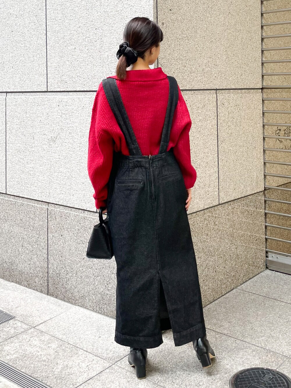 ピンク系のニット/セーター、ブラック系のジャンパースカート、ブラック系のブーツを着用したレディースの冬コーディネートの2枚目の写真