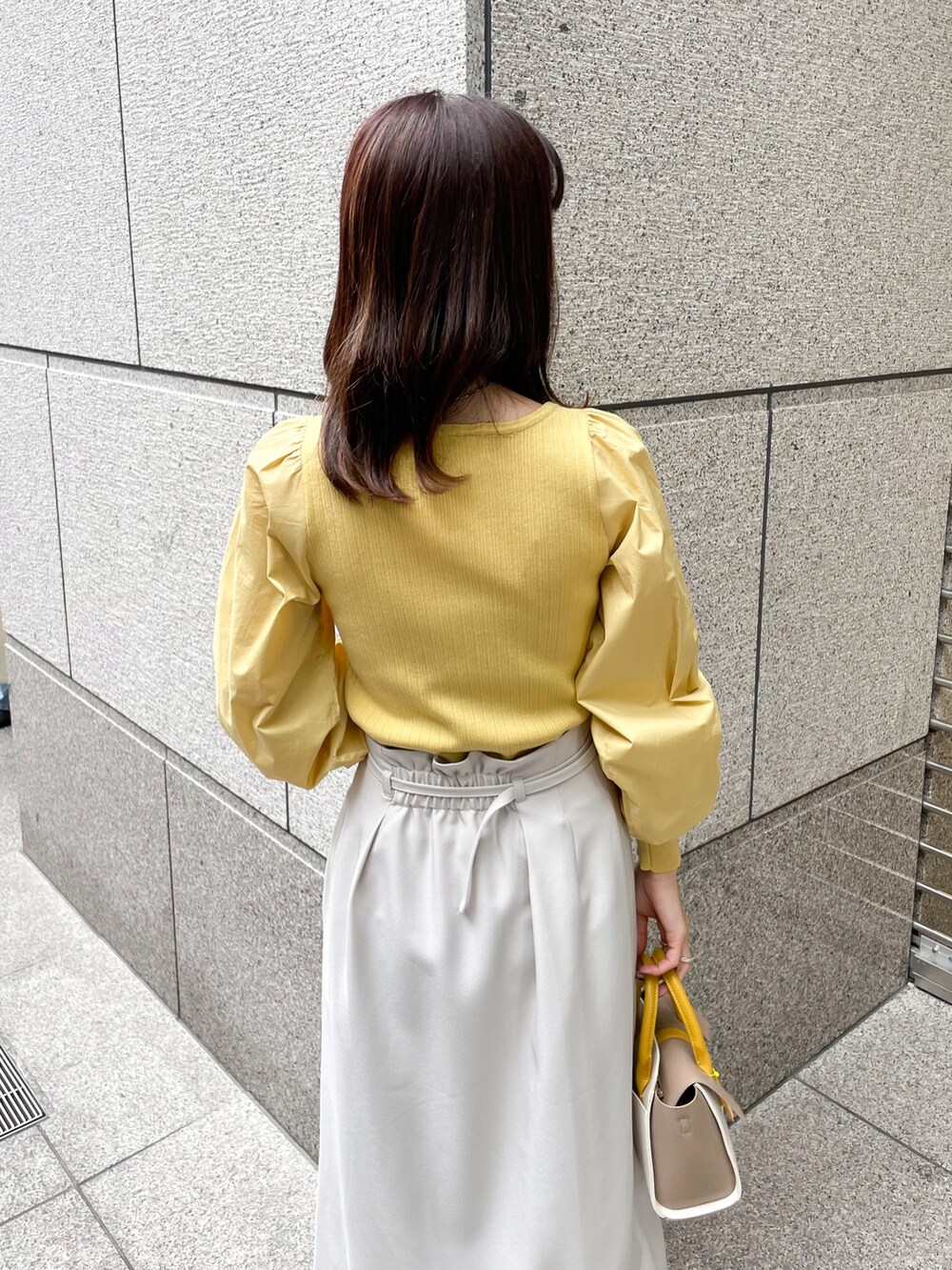 イエロー系のニット/セーター、グレー系のスカート、イエロー系のショルダーバッグを着用したレディースの春コーディネートの5枚目の写真