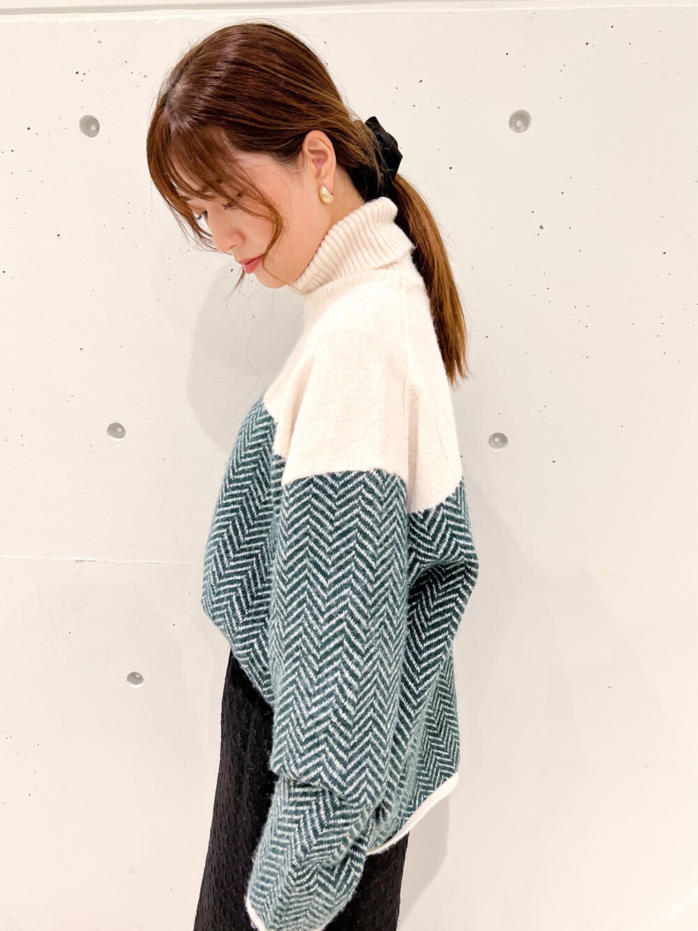 グリーン系のニット/セーター、ブラック系のスカート、ブラック系のショルダーバッグを着用したレディースの秋コーディネートの4枚目の写真