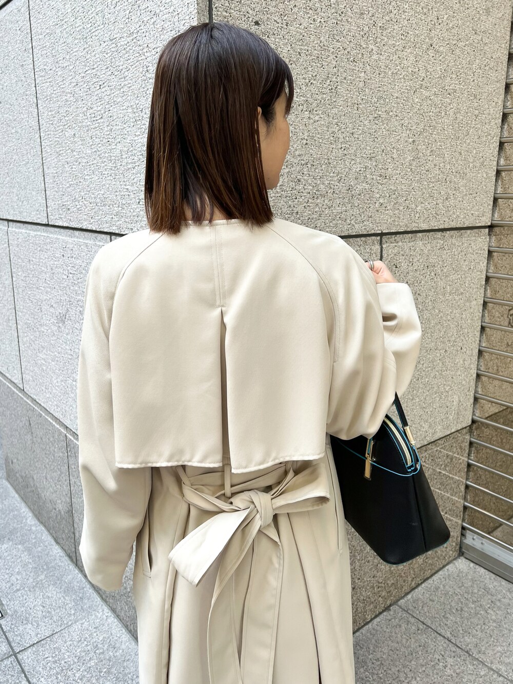 ブルー系のワンピース、ベージュ系のトレンチコート、ブラック系のショルダーバッグを着用したレディースの春コーディネートの4枚目の写真