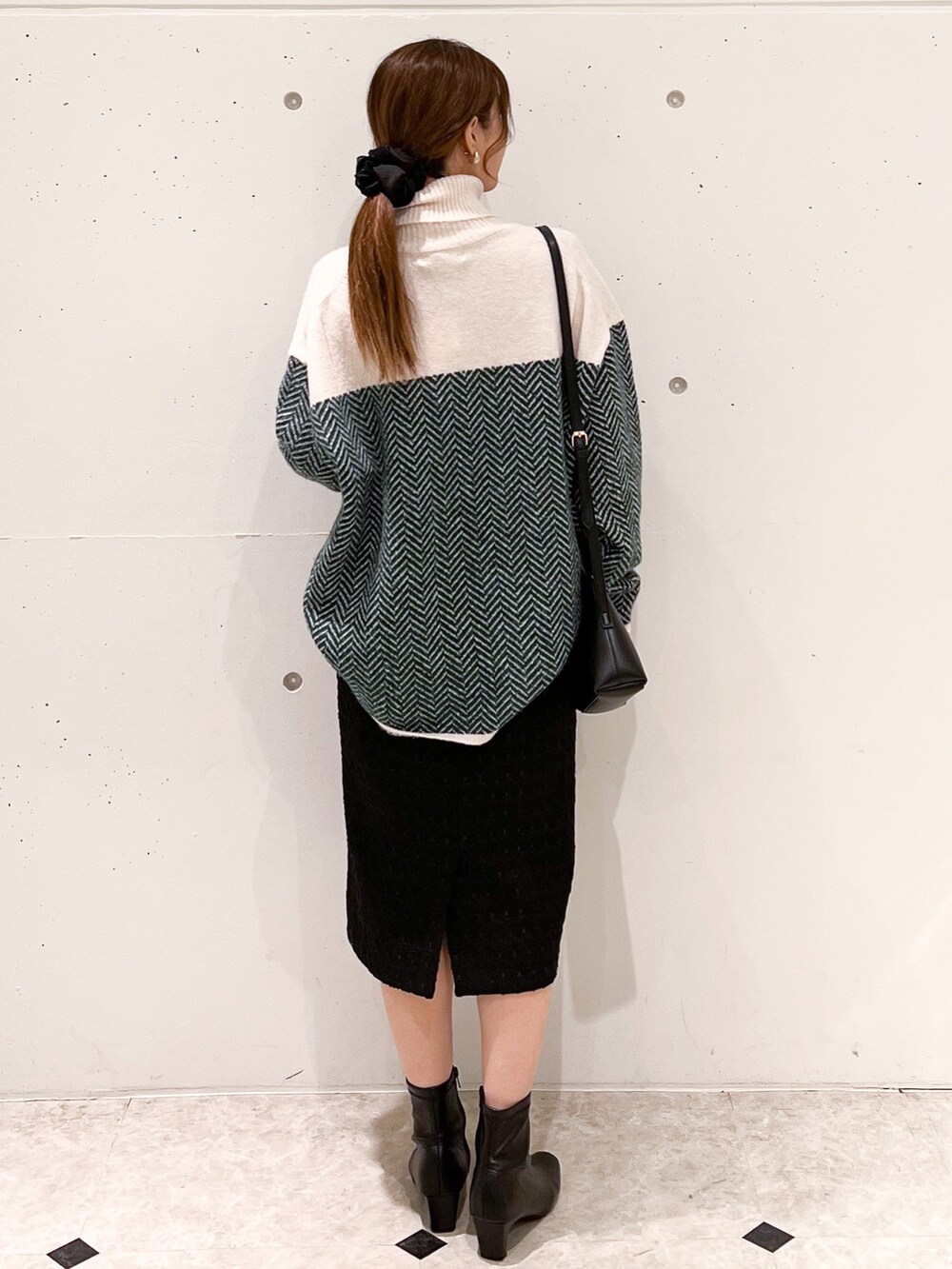 グリーン系のニット/セーター、ブラック系のスカート、ブラック系のショルダーバッグを着用したレディースの秋コーディネートの2枚目の写真