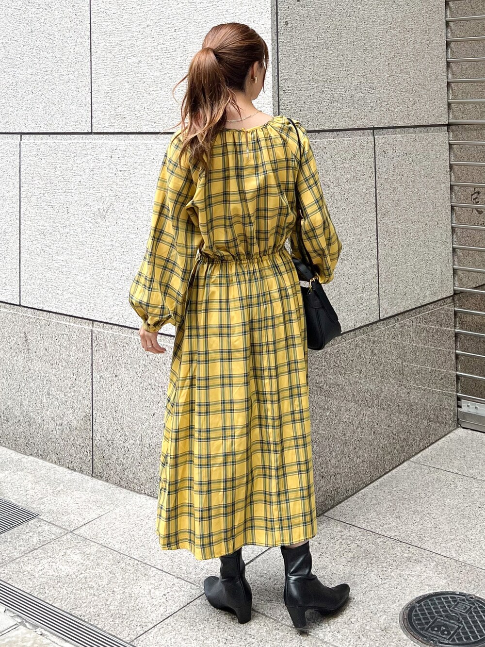 イエロー系のワンピース、ブラック系のショルダーバッグ、ブラック系のブーツを着用したレディースの秋コーディネートの2枚目の写真