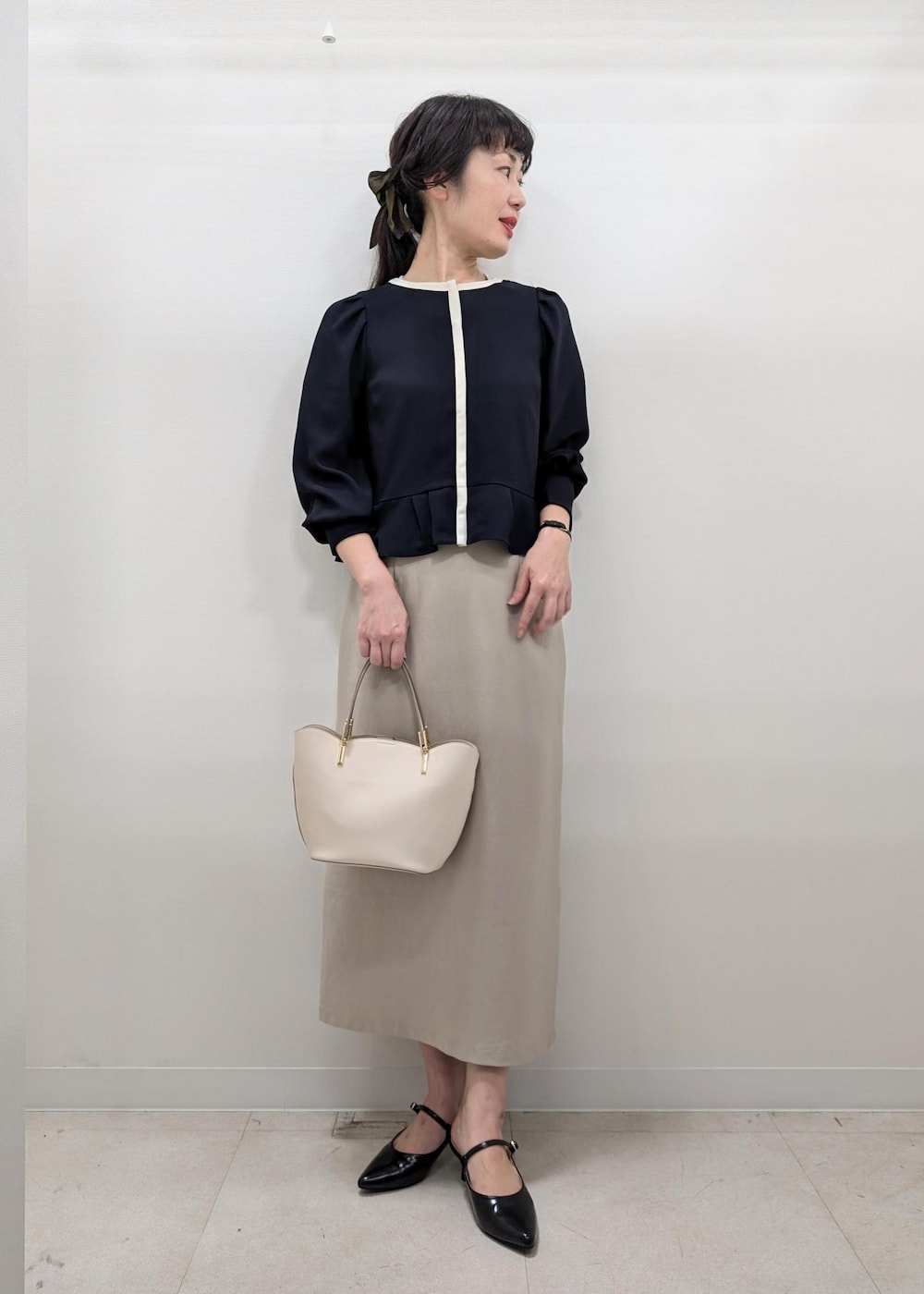 ベージュ系のスカート、ホワイト系のトートバッグ、ブラック系のパンプスを着用したレディースの秋コーディネートの2枚目の写真