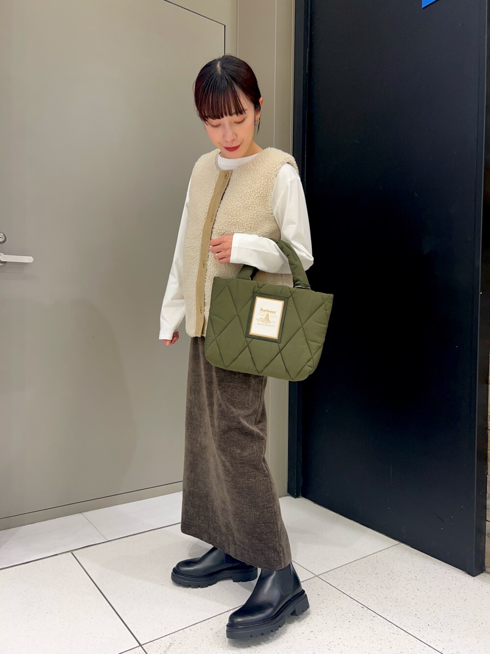 ホワイト系のベスト、ホワイト系のTシャツ/カットソー、ブラウン系のスカートを着用したレディースの秋コーディネートの2枚目の写真