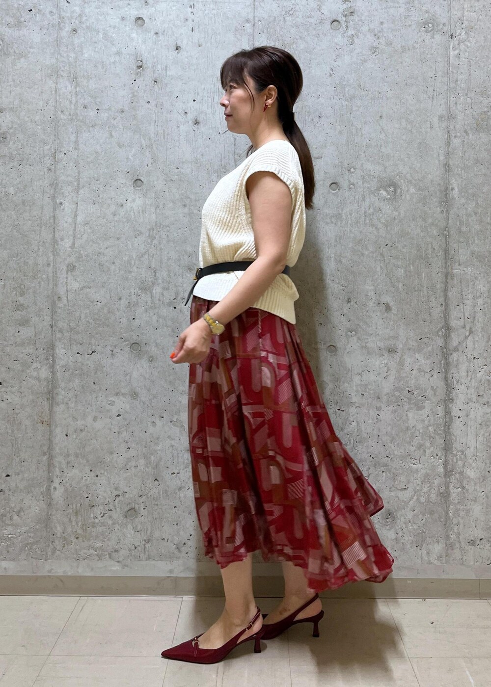 レッド系のパンプス、グレー系のハンドバッグ、ホワイト系のベストを着用したレディースの夏コーディネートの2枚目の写真