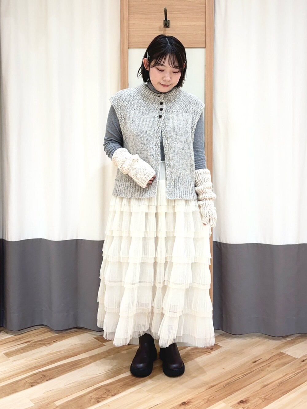 グレー系のベスト、ホワイト系のスカート、ブラウン系のブーツを着用したレディースの秋コーディネートの2枚目の写真