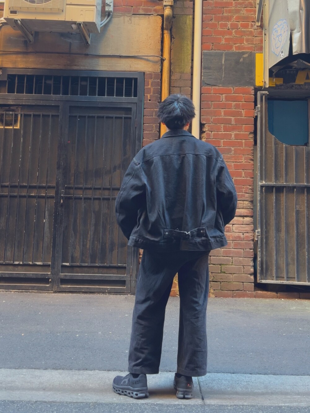 ブラック系のセットアップ、ブラック系のスニーカー、オレンジ系のニット/セーターを着用したメンズの春コーディネートの2枚目の写真