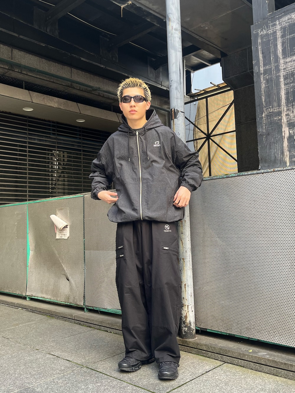 ブラック系のナイロンジャケット、ブラック系のチノパンツ、ブラック系のスニーカーを着用したメンズの春コーディネートの2枚目の写真