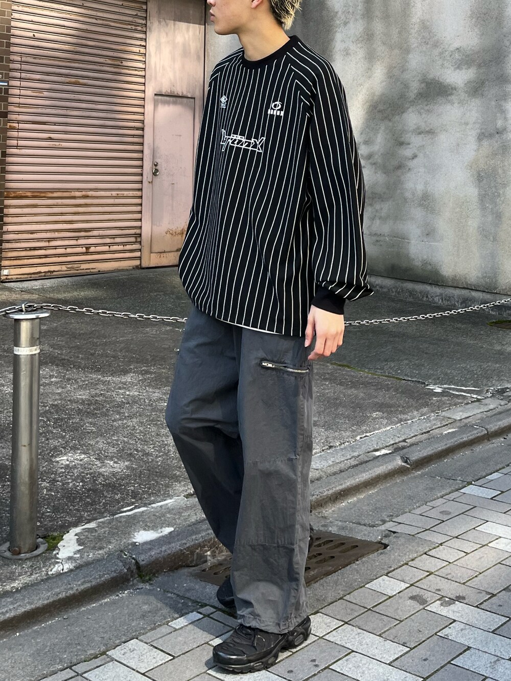 ブラック系のTシャツ/カットソー、グレー系のチノパンツ、ブラック系のスニーカーを着用したメンズの春コーディネートの3枚目の写真