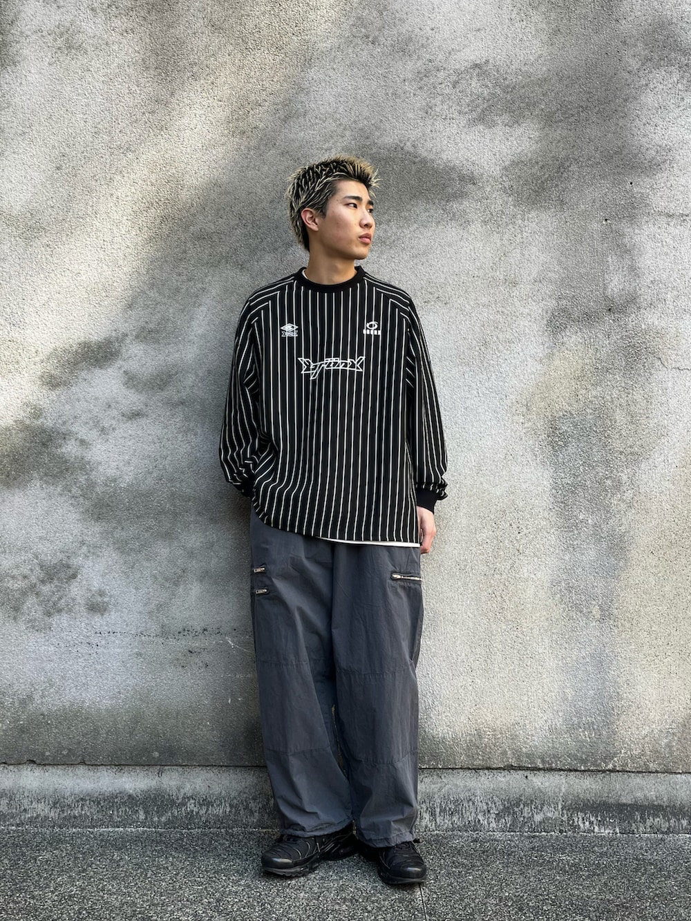 ブラック系のTシャツ/カットソー、グレー系のチノパンツ、ブラック系のスニーカーを着用したメンズの春コーディネートの2枚目の写真