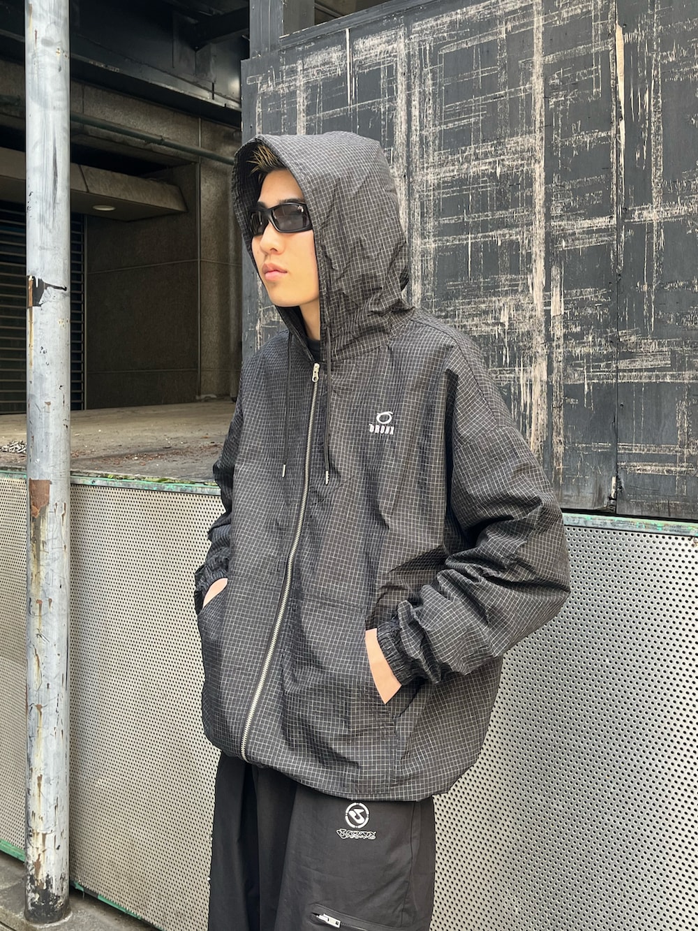 ブラック系のナイロンジャケット、ブラック系のチノパンツ、ブラック系のスニーカーを着用したメンズの春コーディネートの3枚目の写真