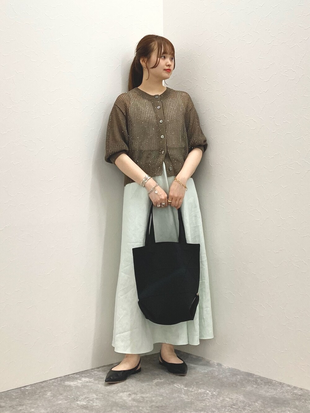 ブラウン系のカーディガン/ボレロ、グリーン系のスカート、ブラック系のショルダーバッグを着用したレディースの春コーディネートの2枚目の写真