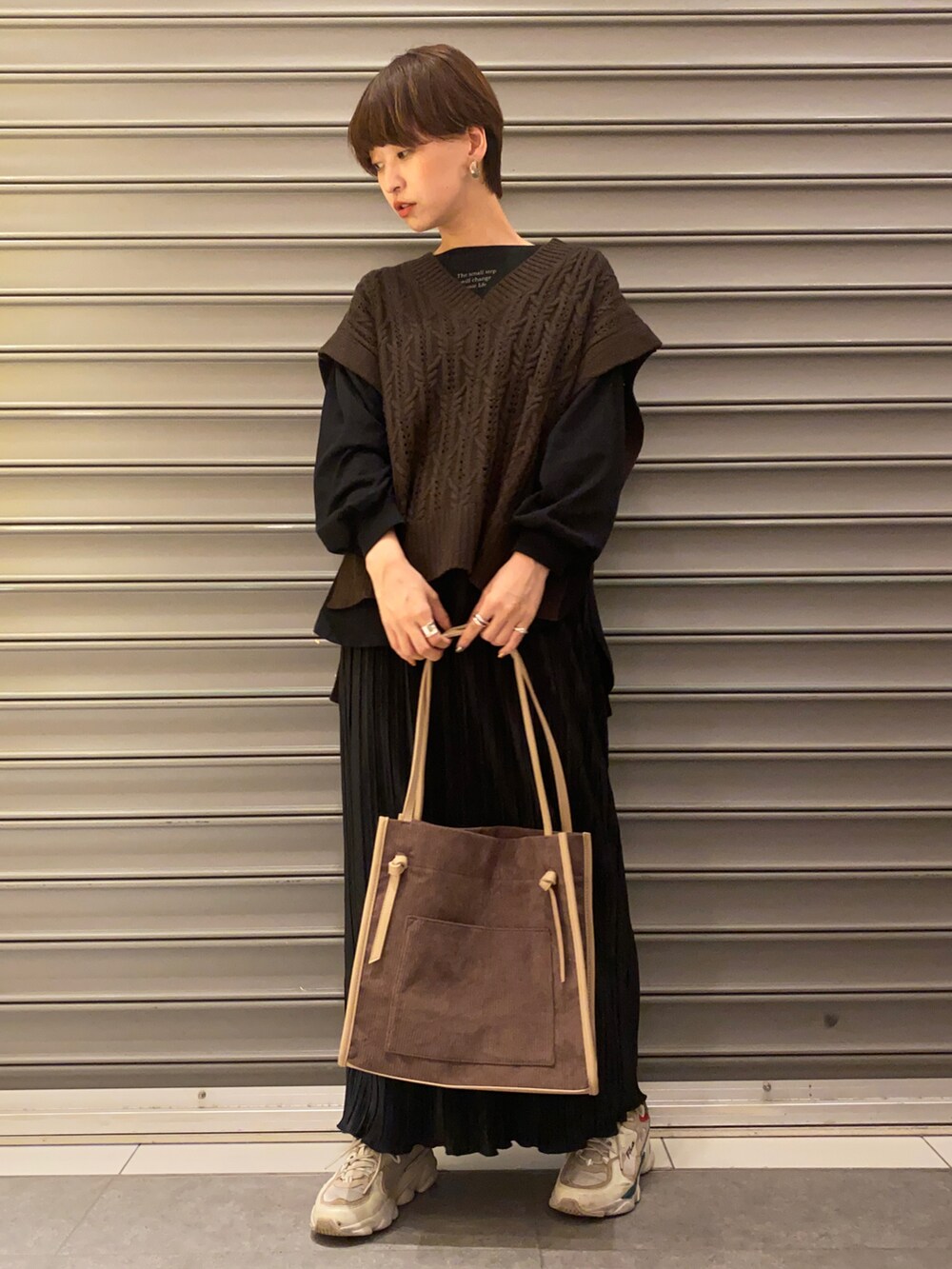 ホワイト系のスニーカー、ブラウン系のベスト、ブラック系のトップスを着用したレディースの秋コーディネートの2枚目の写真