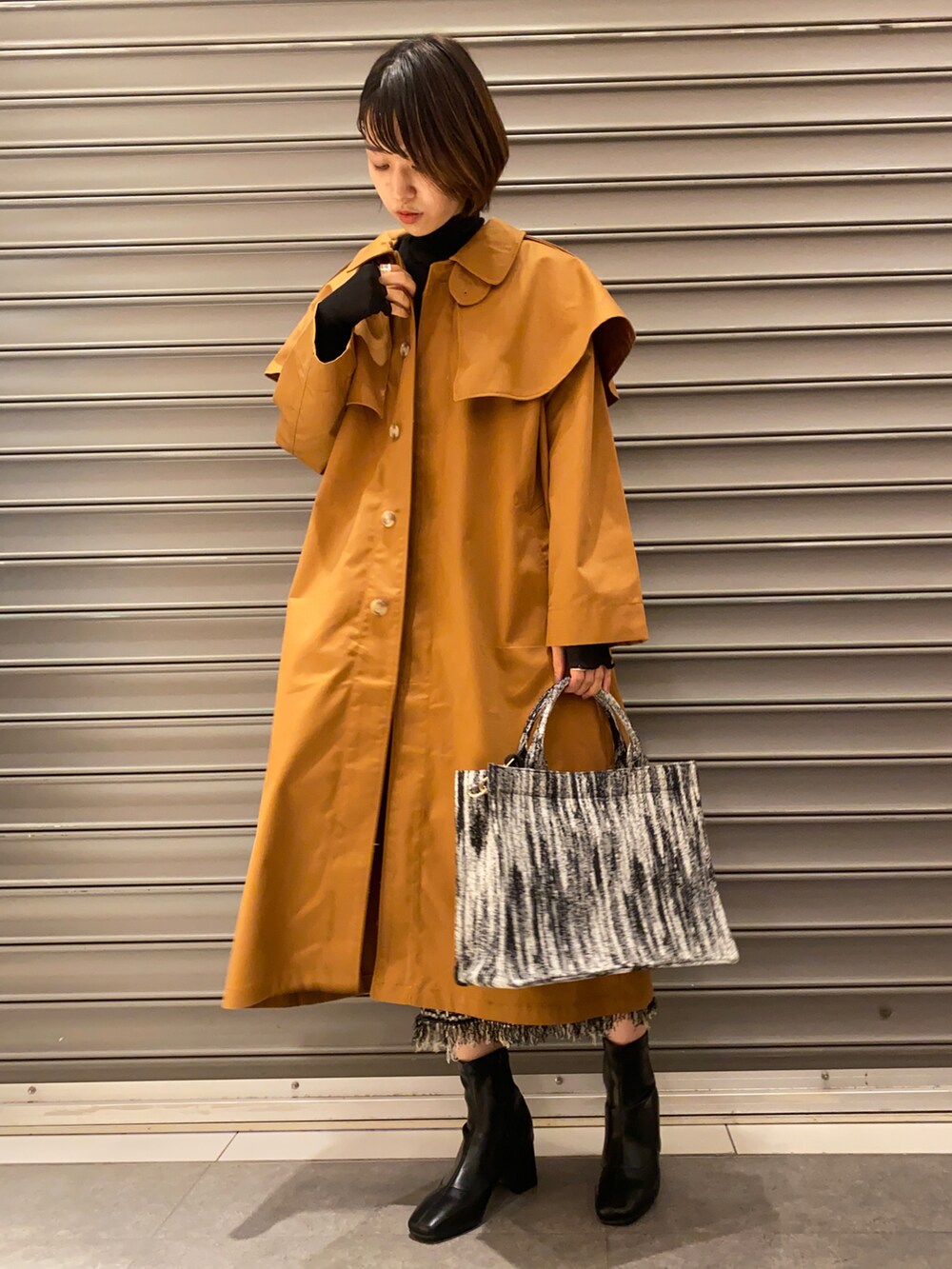 ブラック系のトートバッグ、イエロー系のステンカラーコート、ブラック系のTシャツ/カットソーを着用したレディースの秋コーディネートの3枚目の写真