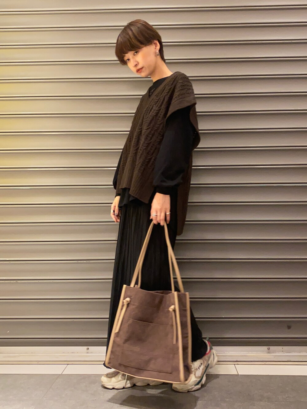 ホワイト系のスニーカー、ブラウン系のベスト、ブラック系のトップスを着用したレディースの秋コーディネートの3枚目の写真