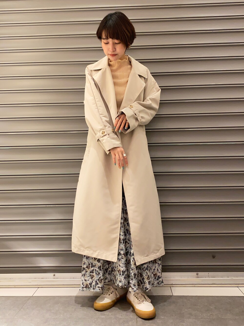 ブルー系のスカート、ホワイト系のスニーカー、ベージュ系のトレンチコートを着用したレディースの春コーディネートの2枚目の写真