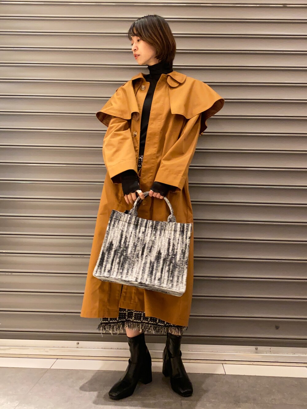 ブラック系のトートバッグ、イエロー系のステンカラーコート、ブラック系のTシャツ/カットソーを着用したレディースの秋コーディネートの2枚目の写真