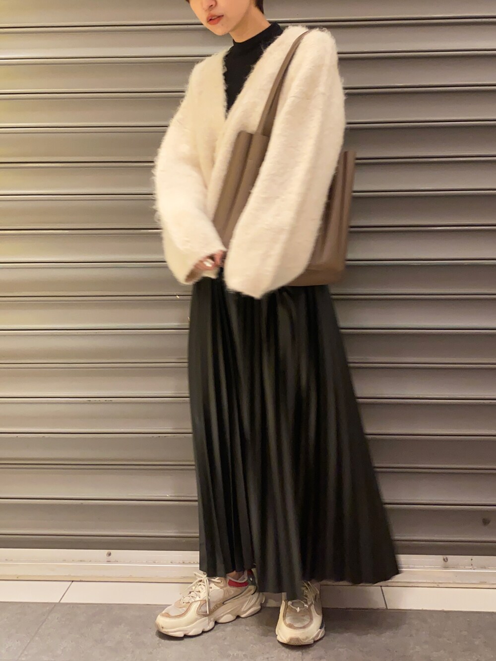 ホワイト系のスニーカー、ホワイト系のカーディガン/ボレロ、ブラック系のスカートを着用したレディースの秋コーディネートの2枚目の写真