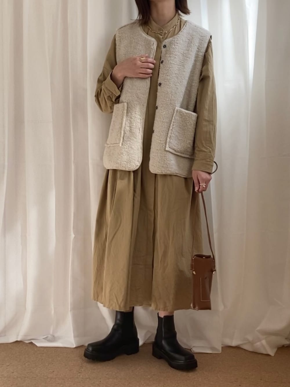 ベージュ系のベスト、ベージュ系のワンピース、イエロー系のショルダーバッグを着用したレディースの秋コーディネートの2枚目の写真