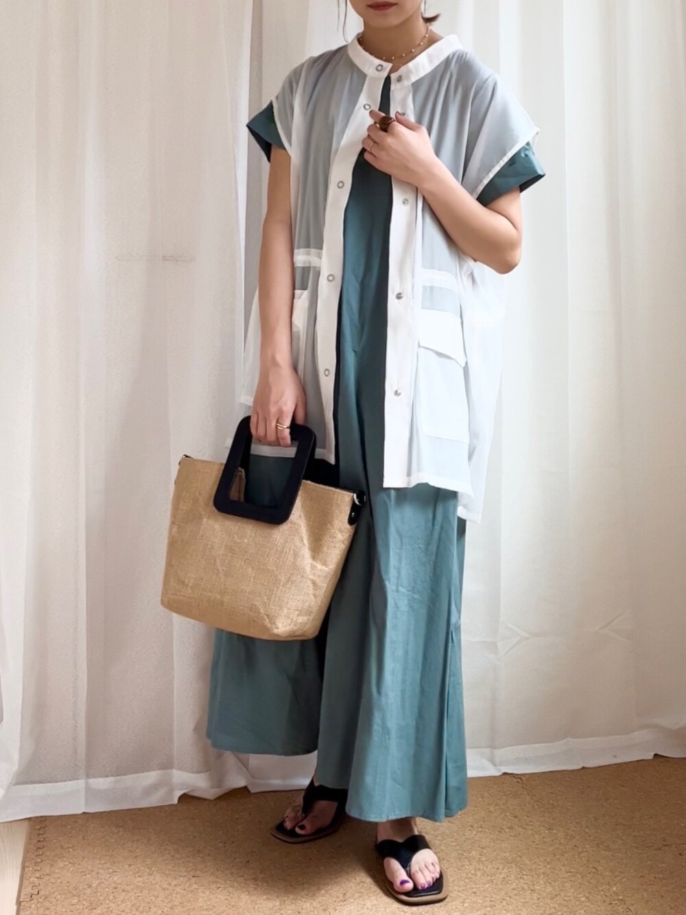 グリーン系のワンピース、ホワイト系のベスト、ブラック系のサンダルを着用したレディースの夏コーディネートの2枚目の写真