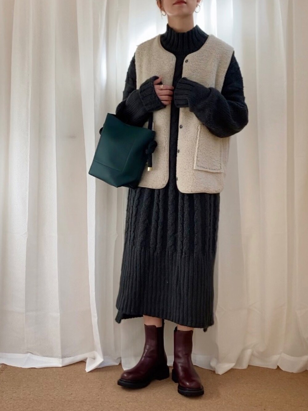 グレー系のワンピース、ベージュ系のベスト、グリーン系のハンドバッグを着用したレディースの冬コーディネートの2枚目の写真