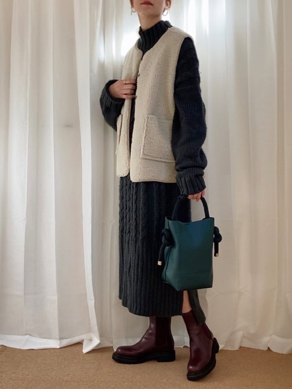 グレー系のワンピース、ベージュ系のベスト、グリーン系のハンドバッグを着用したレディースの冬コーディネートの3枚目の写真