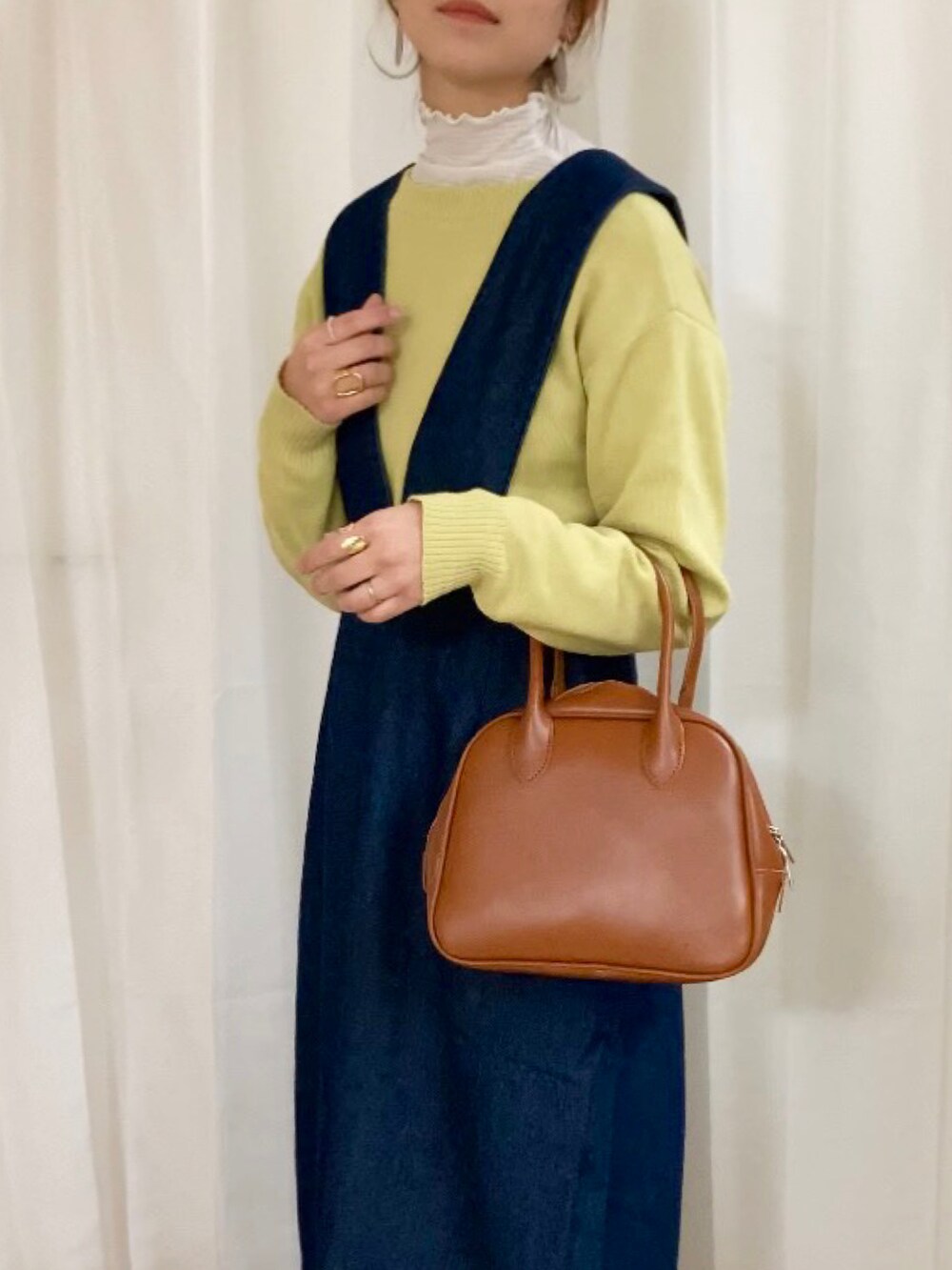 イエロー系のカーディガン/ボレロ、ブルー系のジャンパースカート、イエロー系のボストンバッグを着用したレディースの冬コーディネートの2枚目の写真