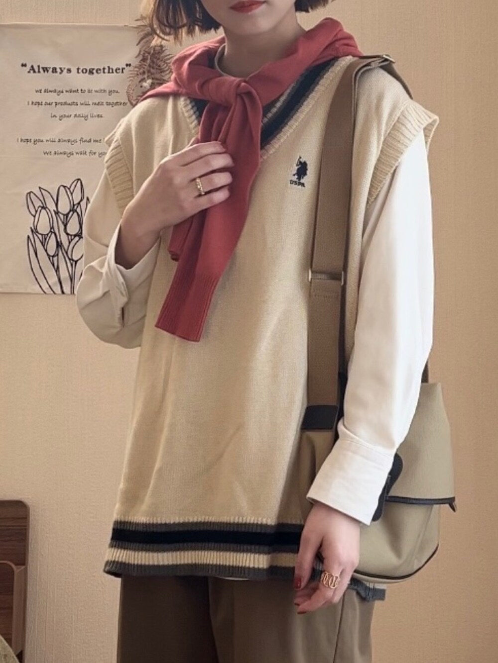 ホワイト系のベスト、グリーン系のチノパンツ、ベージュ系のショルダーバッグを着用したレディースの冬コーディネートの2枚目の写真