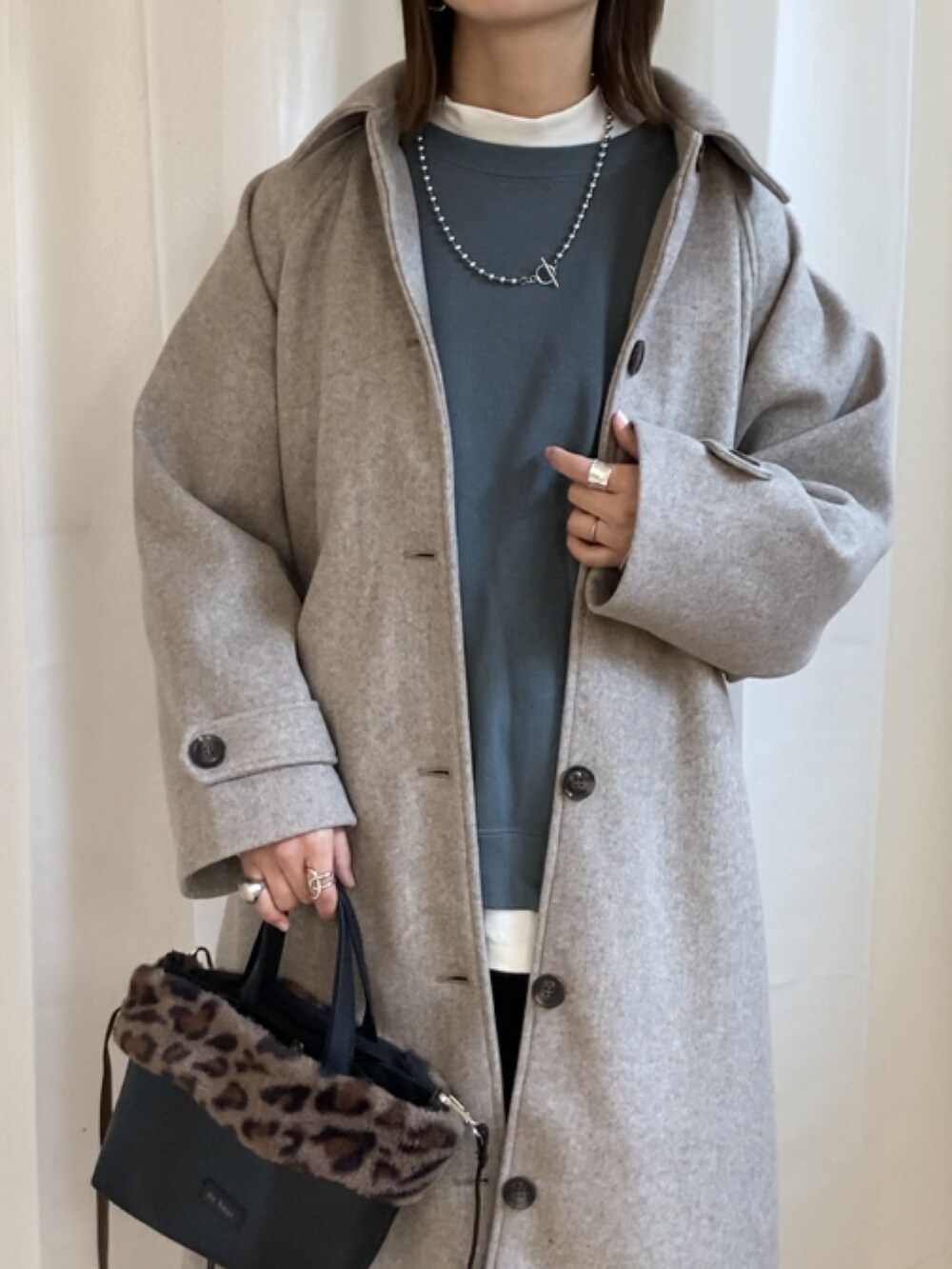 ベージュ系のステンカラーコート、ブルー系のスウェット、ブラック系のその他パンツを着用したレディースの秋コーディネートの2枚目の写真