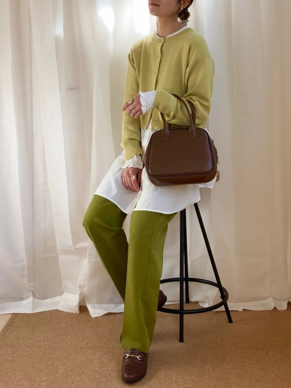 イエロー系のカーディガン/ボレロ、グリーン系のスラックス、ブラウン系のボストンバッグを着用したレディースの冬コーディネートの2枚目の写真