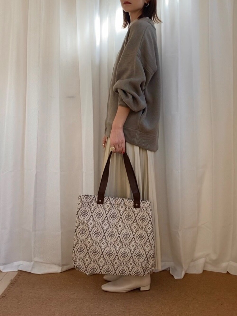 ベージュ系のカーディガン/ボレロ、ホワイト系のスカート、ベージュ系のトートバッグを着用したレディースの冬コーディネートの2枚目の写真