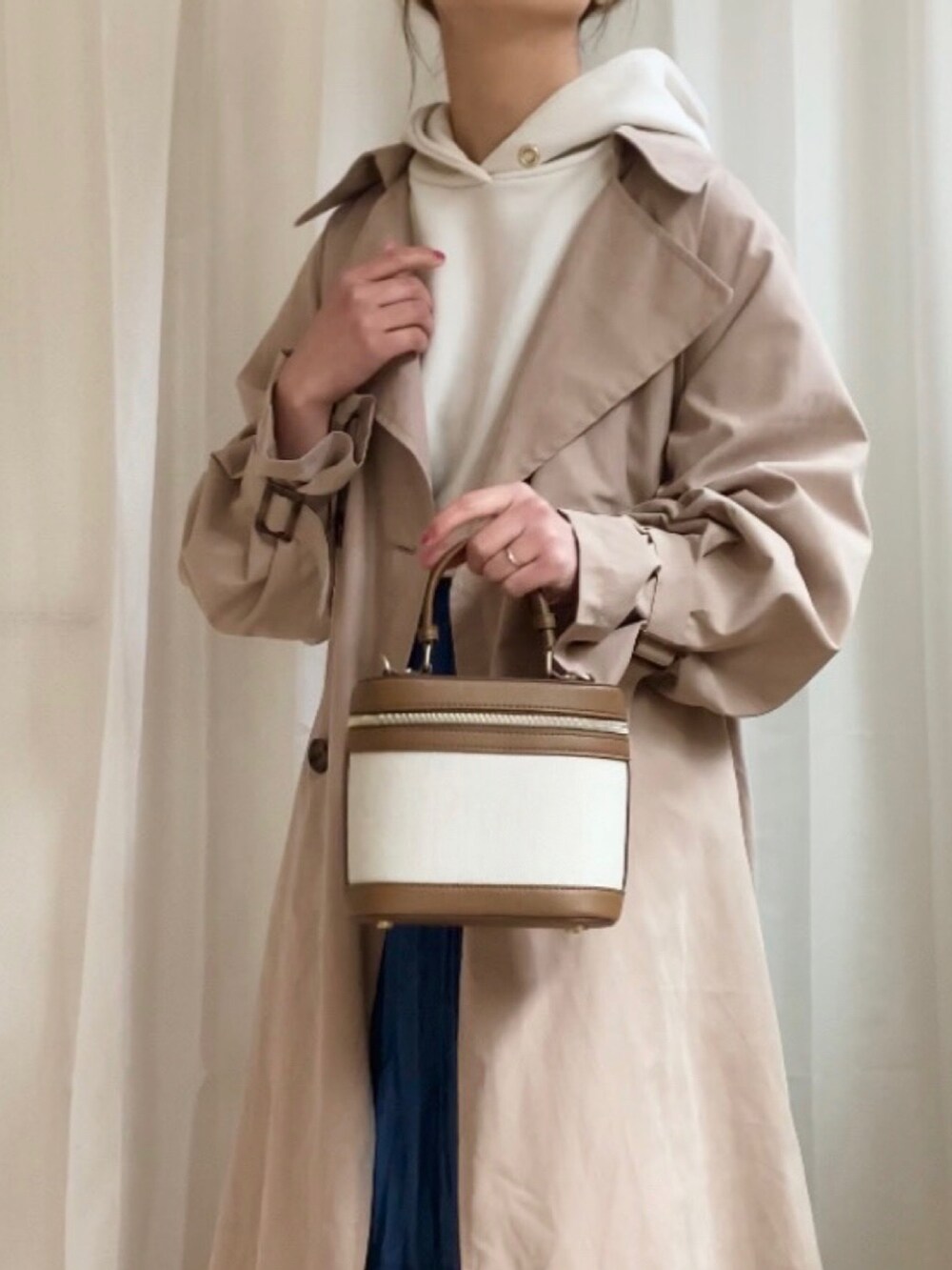 ベージュ系のトレンチコート、ホワイト系のパーカー、ブルー系のデニムスカートを着用したレディースの冬コーディネートの2枚目の写真