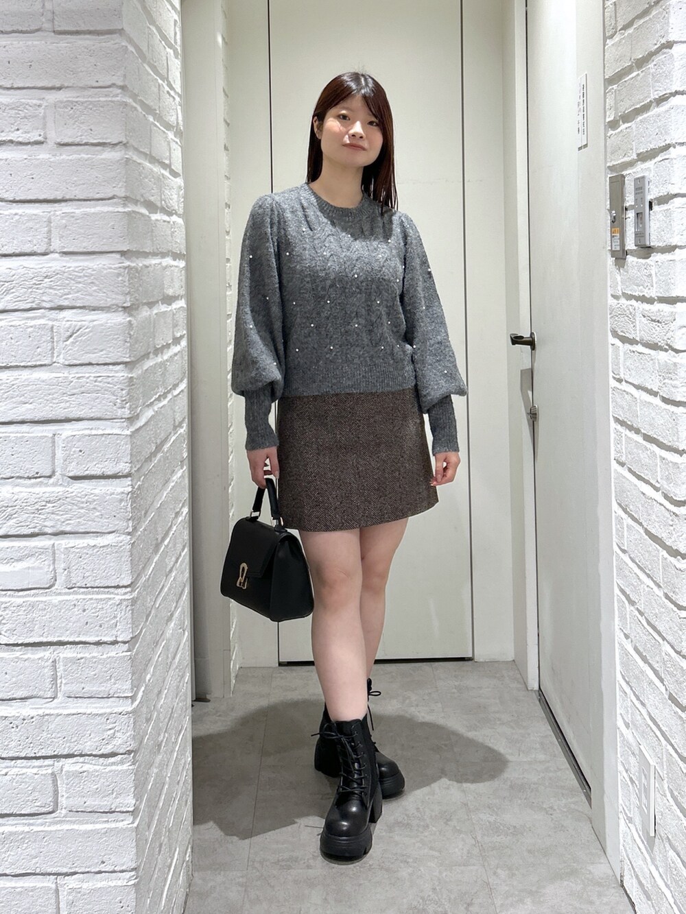 ブラック系のトートバッグ、ブラック系のブーツ、ブラウン系のスカートを着用したレディースの秋コーディネートの2枚目の写真