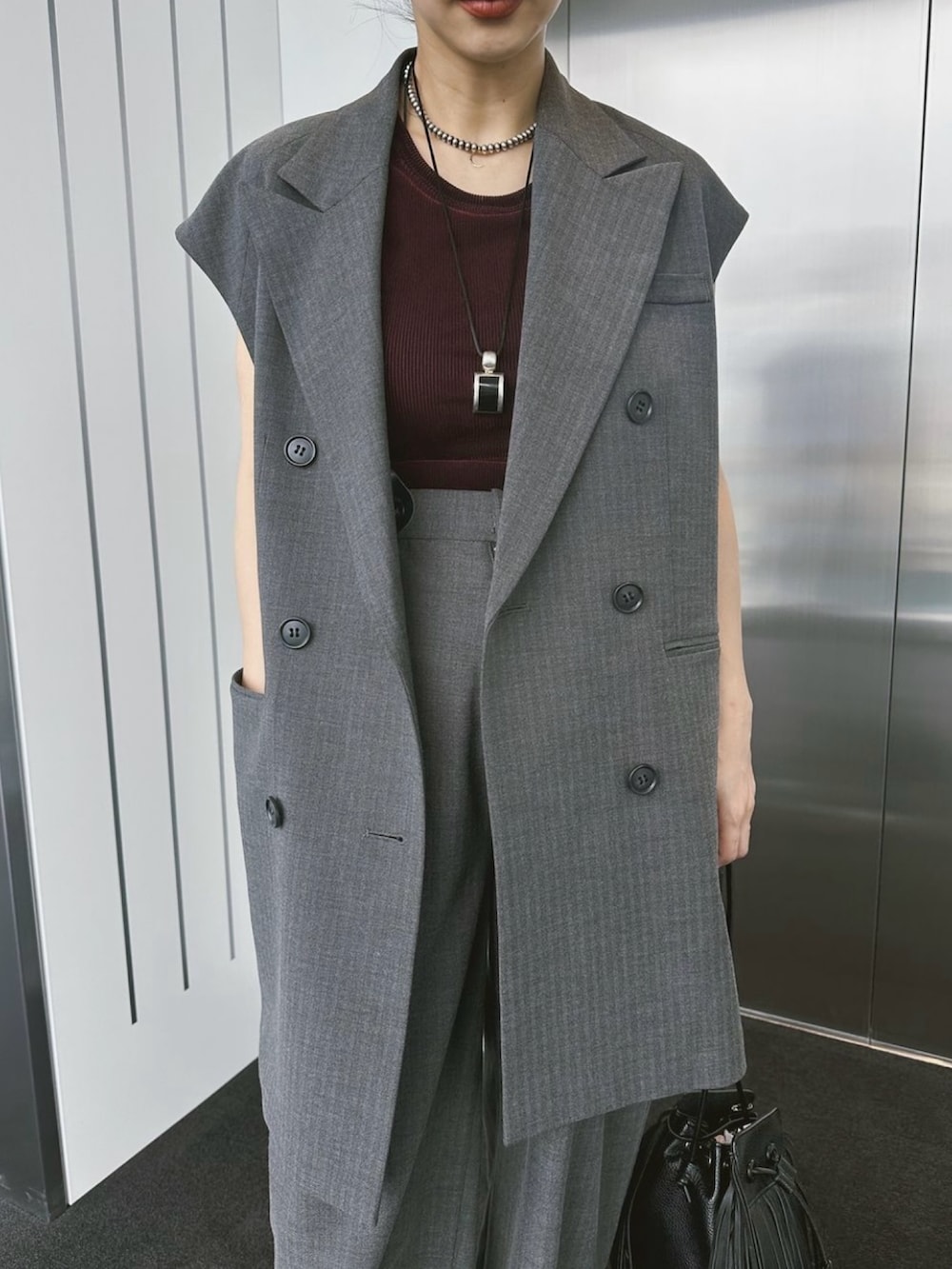 レッド系のタンクトップ、グレー系のベスト、ブラック系のショルダーバッグを着用したレディースの夏コーディネートの3枚目の写真