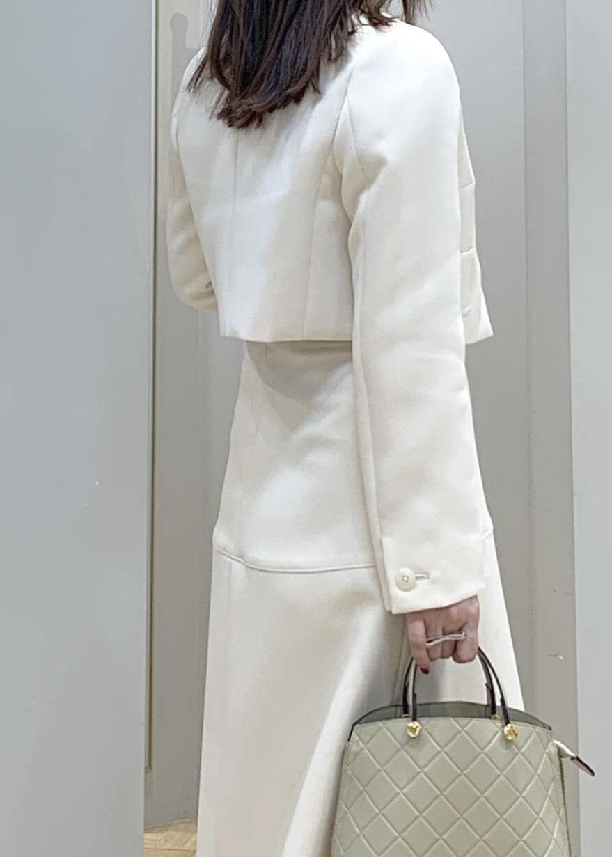 ブラック系のパンプス、ベージュ系のハンドバッグ、ホワイト系のスカートを着用したレディースの冬コーディネートの3枚目の写真