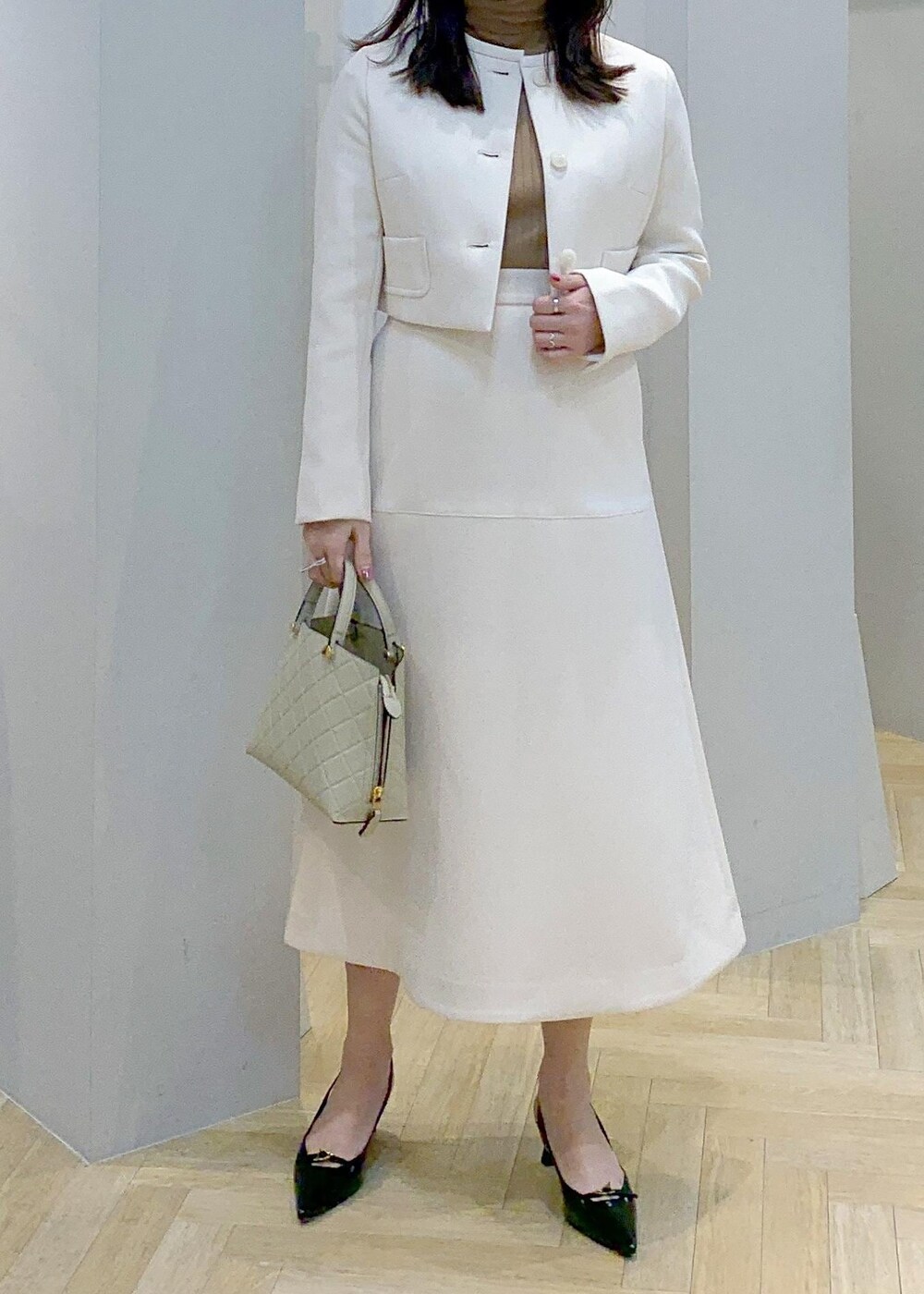 ブラック系のパンプス、ベージュ系のハンドバッグ、ホワイト系のスカートを着用したレディースの冬コーディネートの2枚目の写真