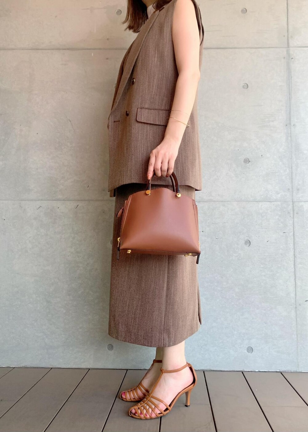 ブラウン系のハンドバッグ、ブラウン系のベスト、ホワイト系のTシャツ/カットソーを着用したレディースの夏コーディネートの3枚目の写真