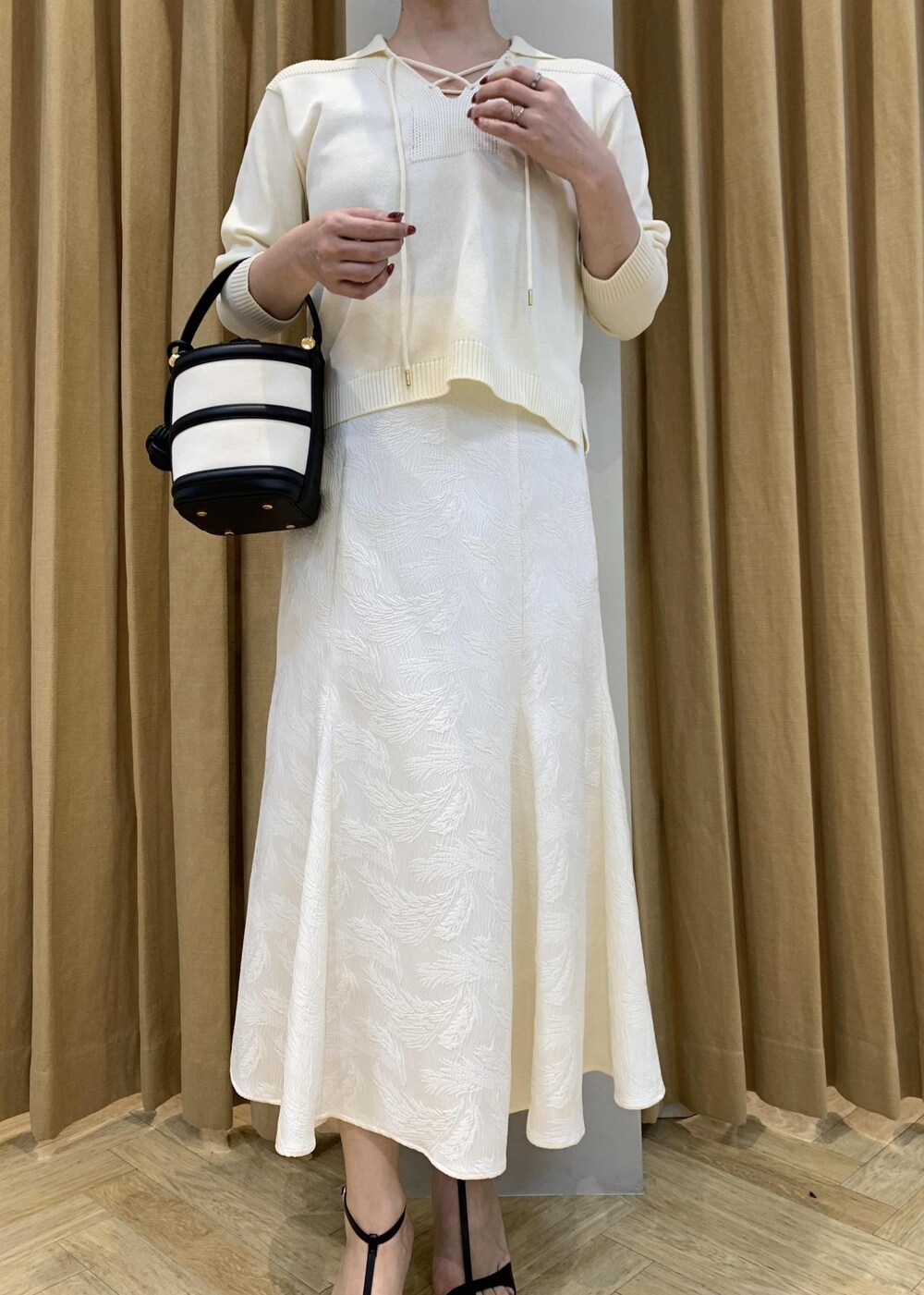 ブラック系のハンドバッグ、ブラック系のサンダル、ホワイト系のニット/セーターを着用したレディースの春コーディネートの2枚目の写真