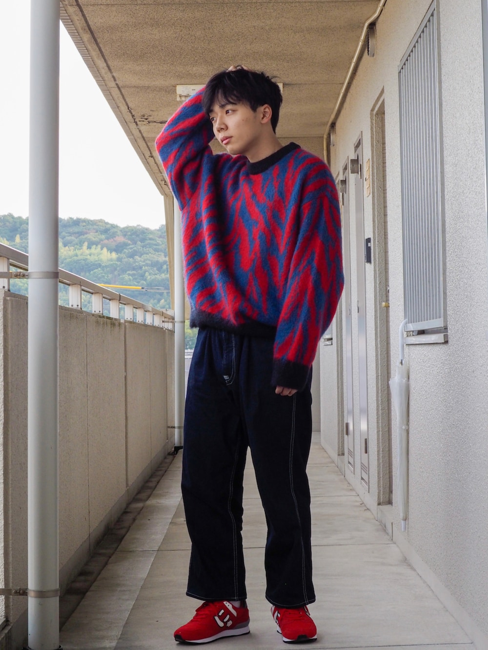 レッド系のニット/セーター、ブルー系のデニムパンツ、レッド系のスニーカーを着用したメンズの秋コーディネートの2枚目の写真