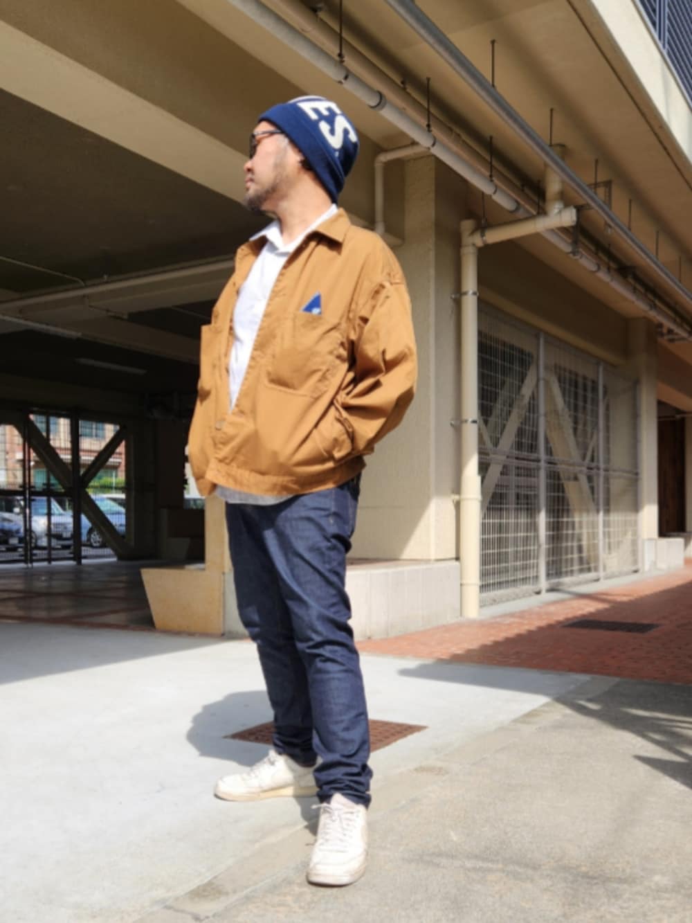 ブルー系のデニムパンツ、ホワイト系のスニーカー、ブラウン系のブルゾンを着用したメンズの春コーディネートの3枚目の写真