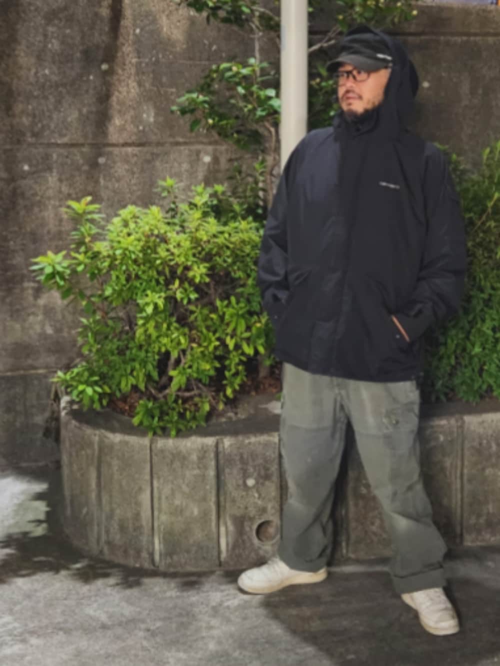 ホワイト系のスニーカー、グリーン系のチノパンツ、ブラック系のナイロンジャケットを着用したメンズの春コーディネートの2枚目の写真